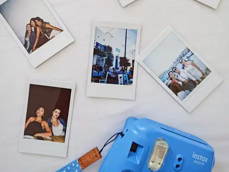Des polaroids étalés sur un lit à côté d'un appareil instantané.