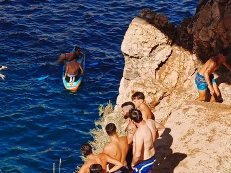 Des baigneurs sur les rochers au bord d'une eau très bleue.